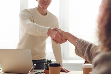 Two people shaking hands in a professional setting, symbolizing a win-win situation in coaching where mutual benefits and positive outcomes are achieved for both coach and client.