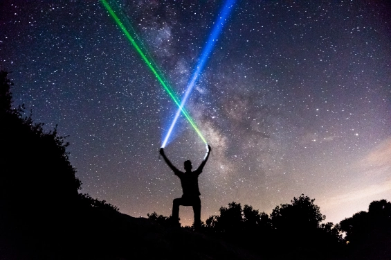 Silhouette of a person holding green and blue light beams against a starry sky, symbolizing gaining visibility and building a strong reputation in the coaching market.