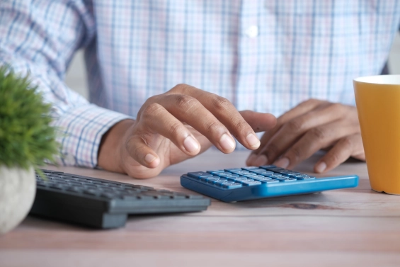 Close-up of a person using a calculator at a desk, symbolizing the concept of creating additional income through skills, knowledge, and passion in coaching.