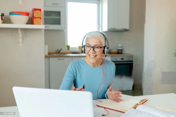 Smiling older woman coach conducting an online coaching session from home, wearing a headset and engaging with a client, symbolizing the positive impact and transformation coaches bring.