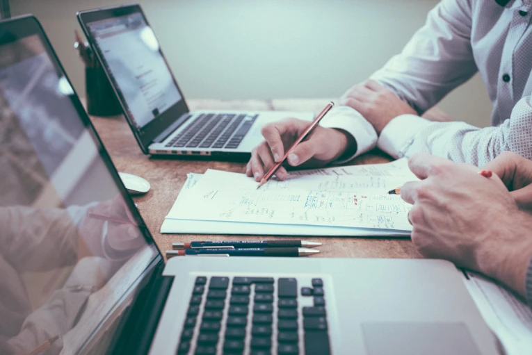 Two professionals collaborating over laptops and documents, symbolizing the creation of tailored coaching sessions designed to address specific challenges within the Coaching Network.