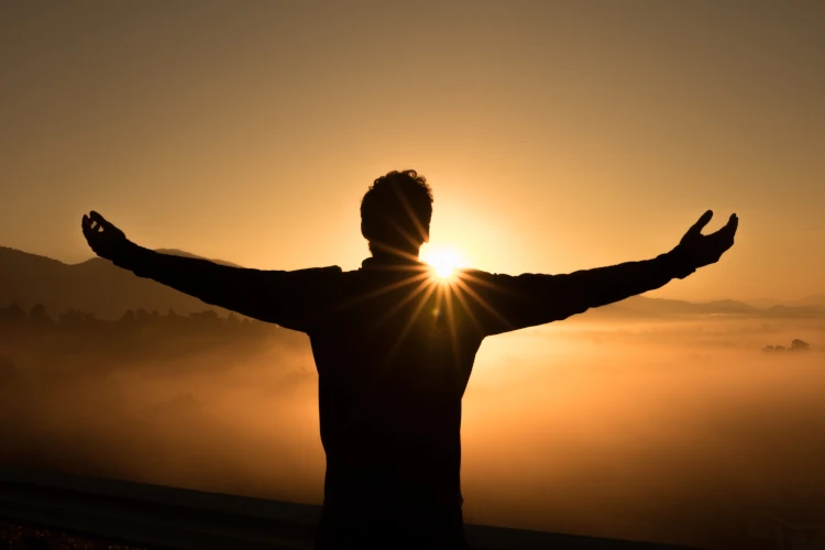 Silhouette of a person with arms outstretched facing the sunrise, symbolizing the power of coaching to inspire personal growth, confidence, and a fresh start toward achieving goals.